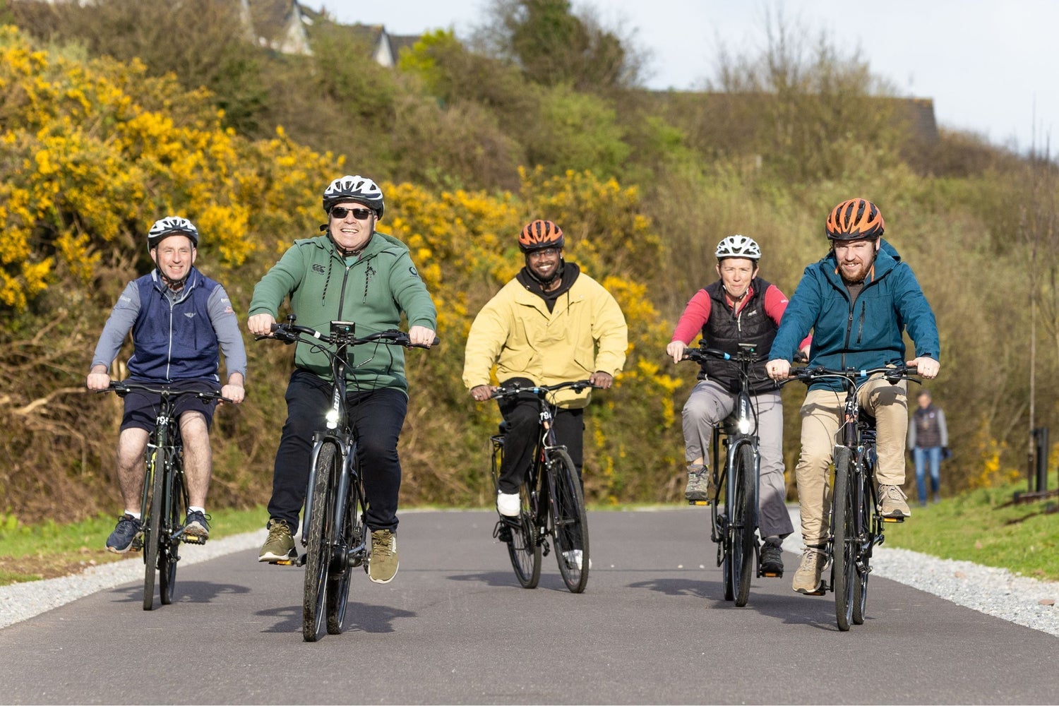 A group cycling on a country road with colourful bushes in the background