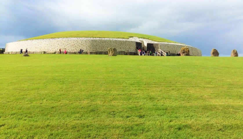 An image of Newgrange with green grass in foreground and a backdrop of a moody grey sky