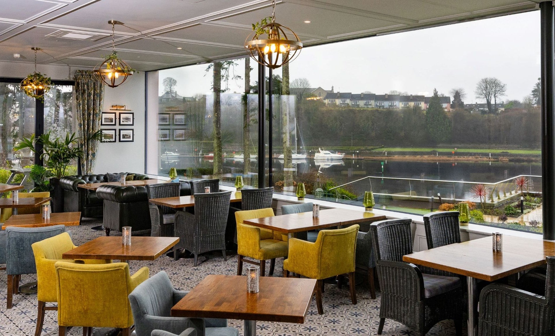 Interior of a restaurant with tables grey and yellow chairs and a window overlooking water