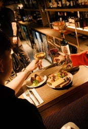Table with plates of food and two people each holding a wine glass