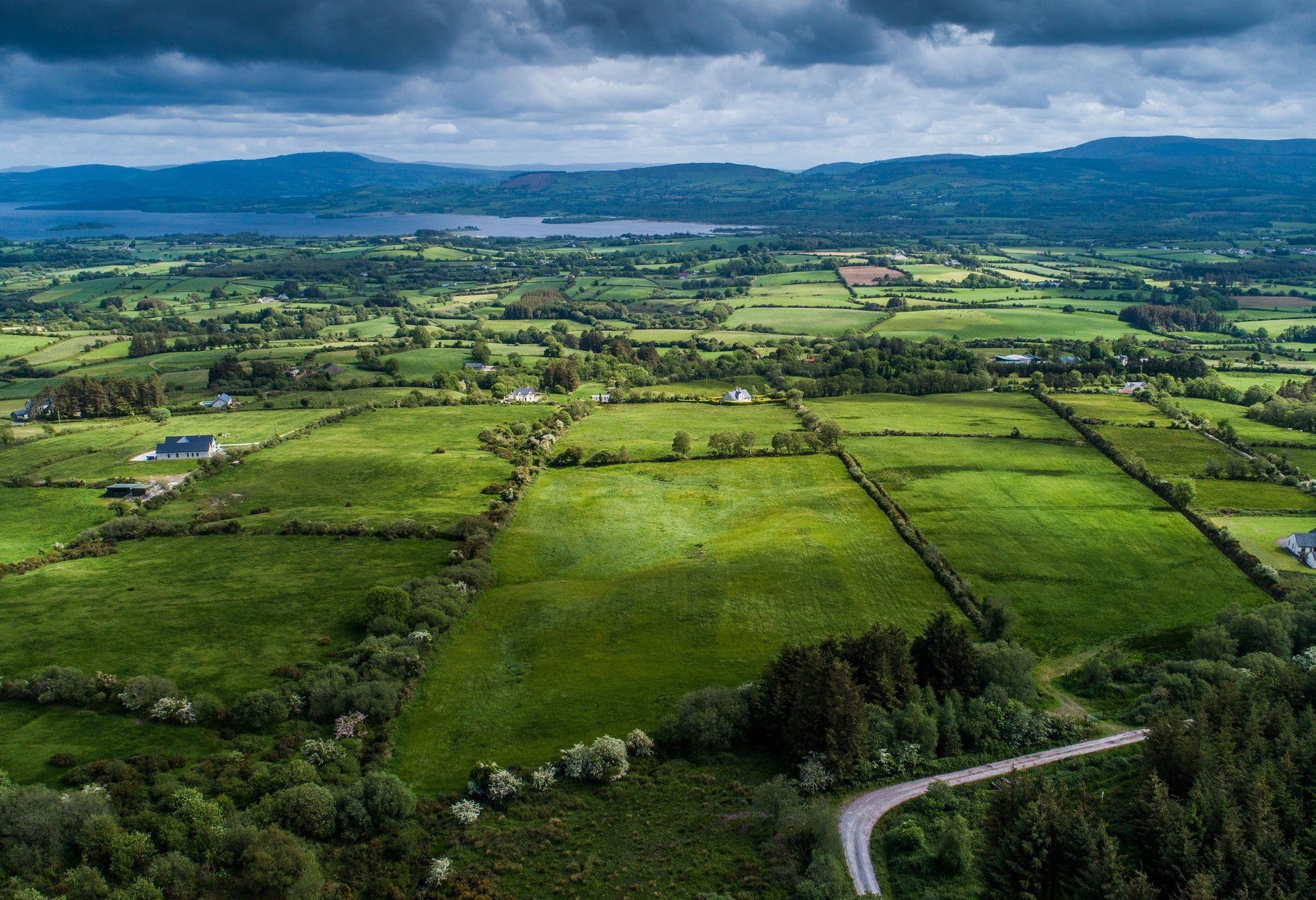 Aerial view of green fields a lake and mountains with a cloudy sky