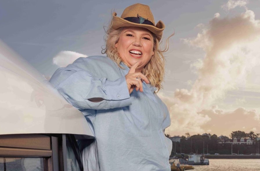 A laughing woman wearing a brown cowboy style hat outdoors with harbour in background.