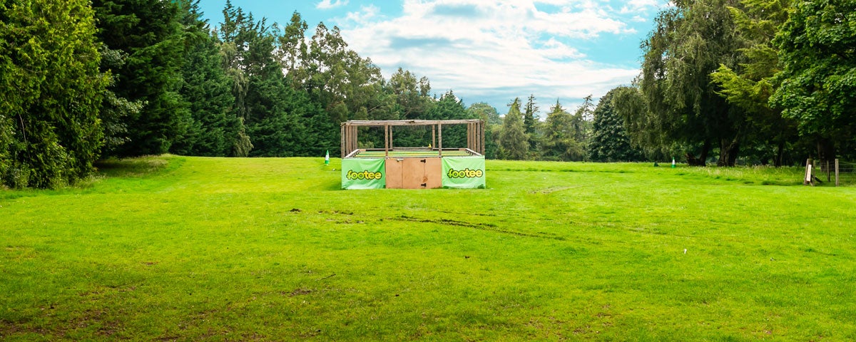 A green field area surrounded by trees with a wooden structure in the distance