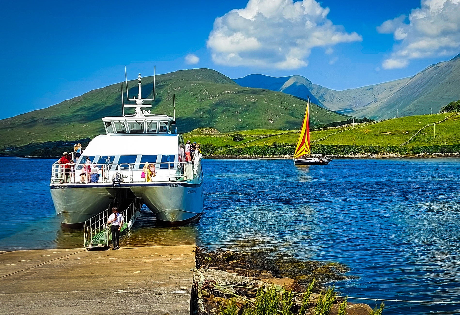 White boat docked at a slipway with green mountains in the background