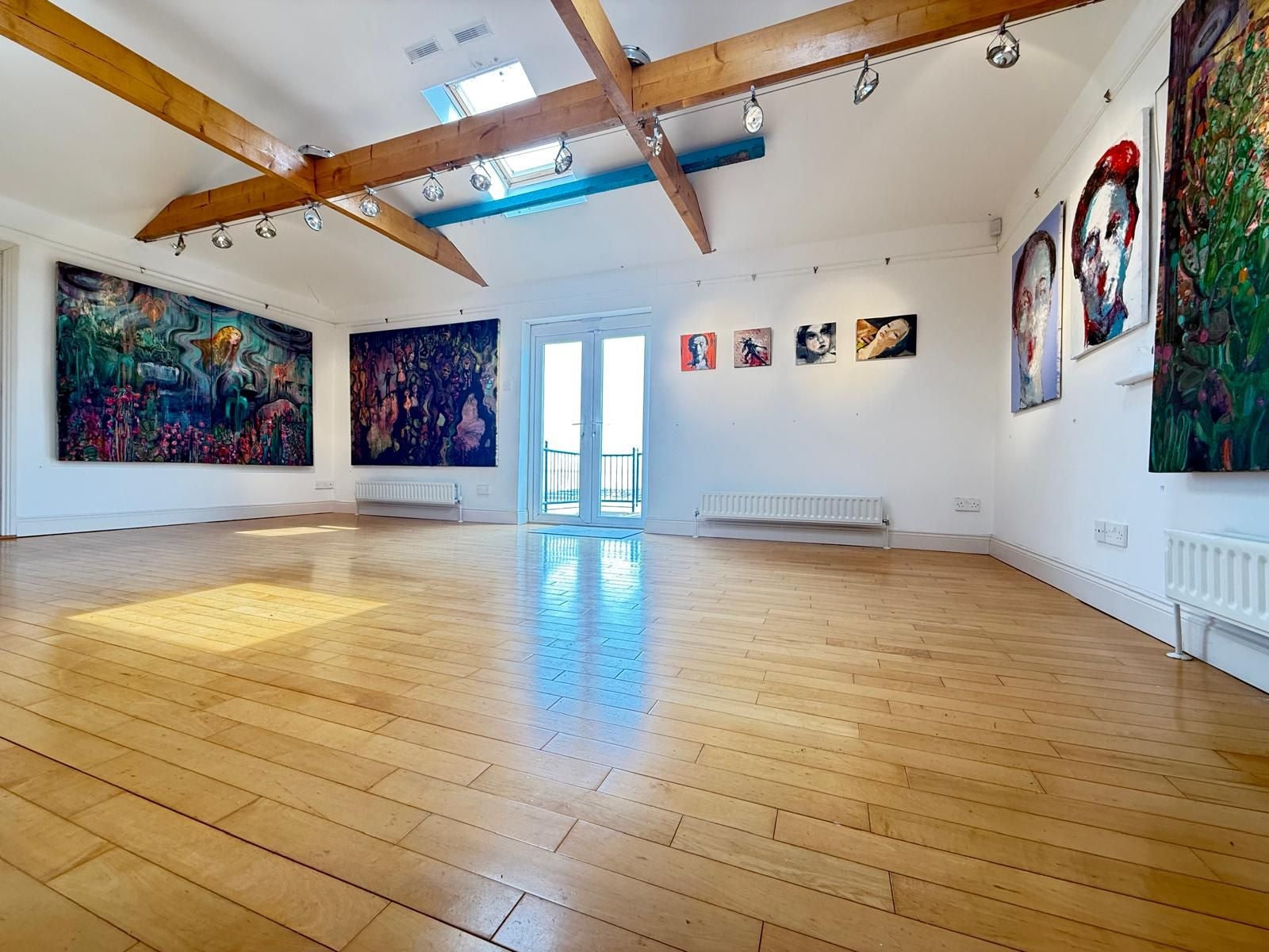 A large room with wooden flooring and white walls with artworks on display