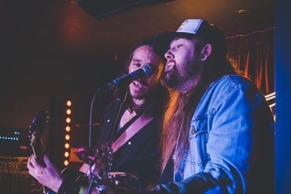 Walker Tex & Wilson Lyons playing guitars and singing into the one mic on a stand.
