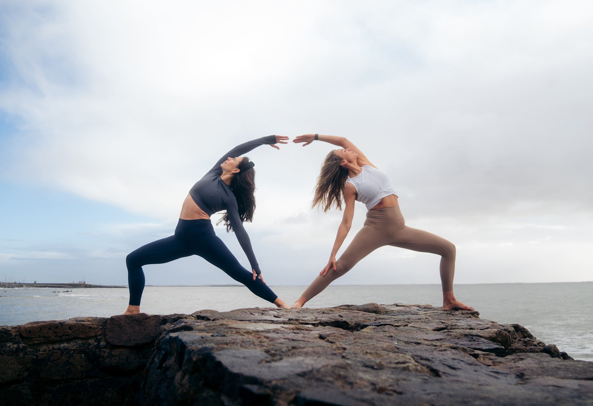 Two people doing yoga stretches on rocks next to the sea