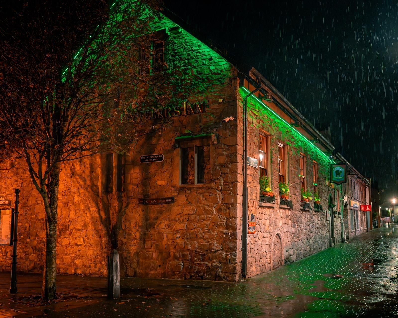 Exterior of a stone building at night with green strip lighting underneath the roof
