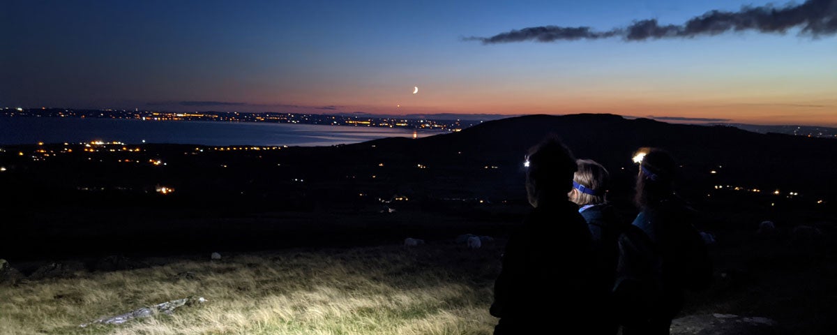 Three walkers on the Cooley Mountains at dusk overlooking the lough