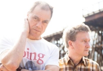 2 men outside with tall structure in background.