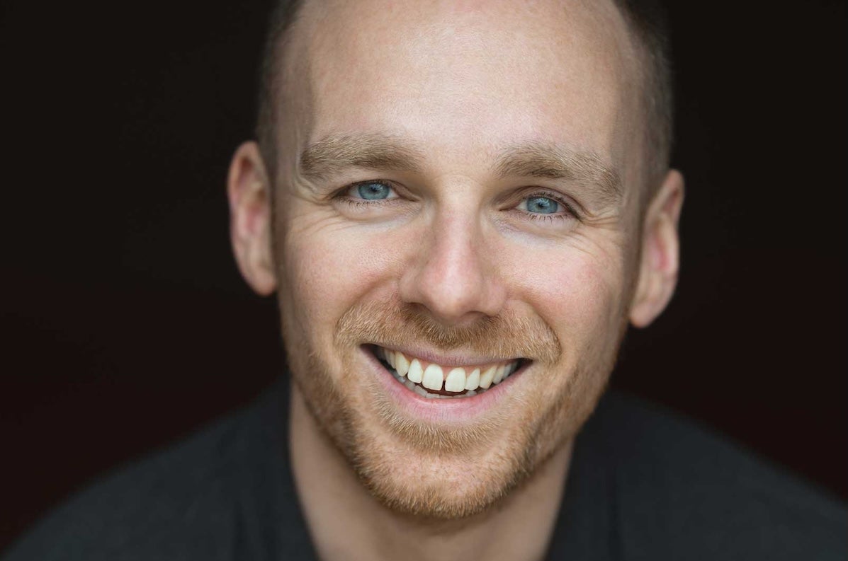 Close up view of man's face, smiling against black background.