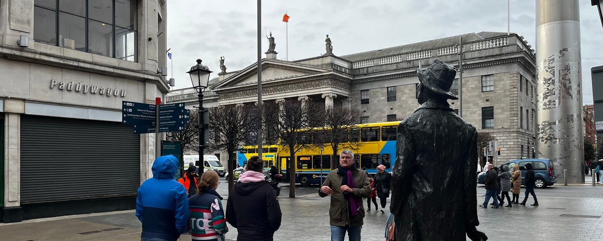 A group of people and a tour guide at a statue in Dublin