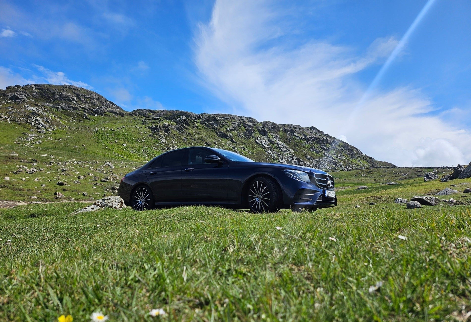 Luxury car parked among greenery with mountains in the background