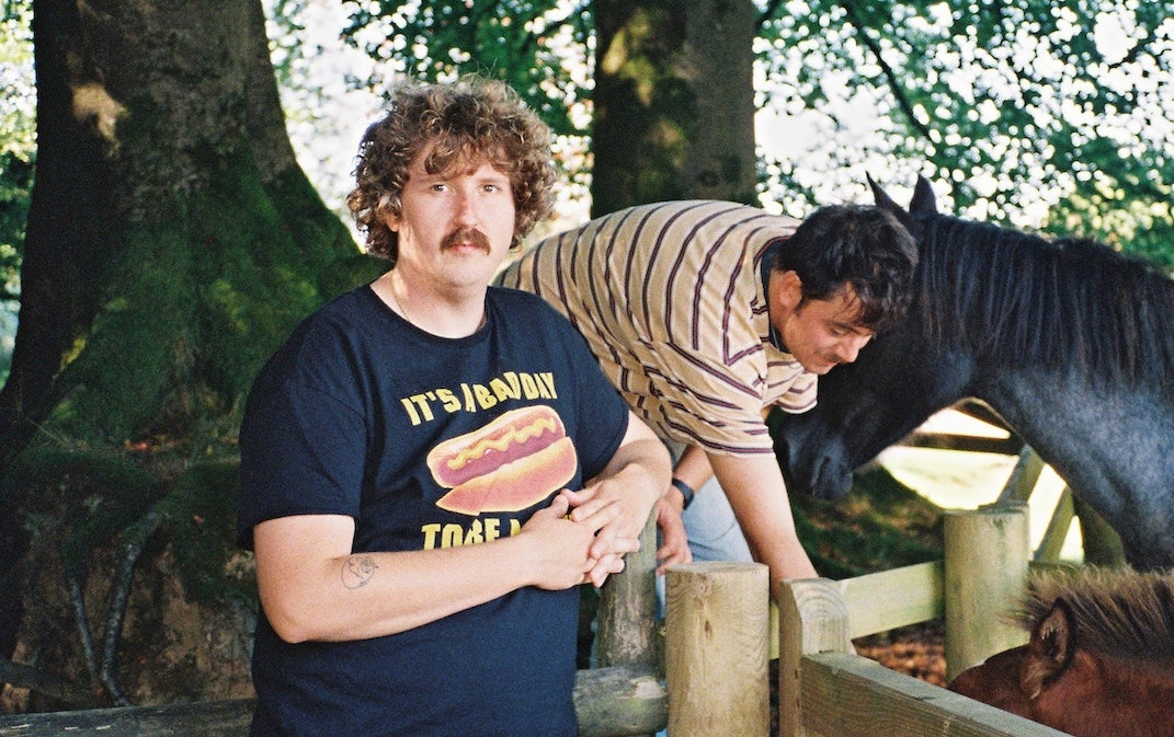 2 people outdoors beside wooden fence holding back horses