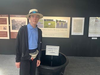 Person standing beside a black soup pot from the famine with storyboards in the background