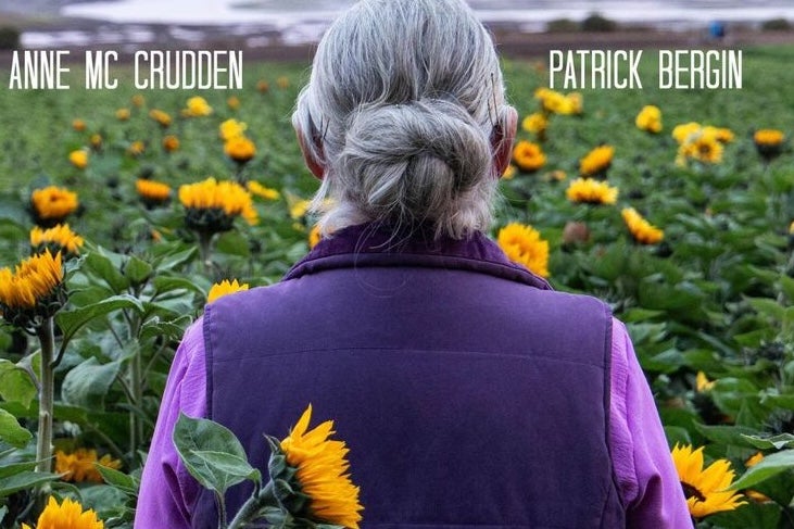 Film poster showing rear view of women in purple jacket standing in a field of sunflowers