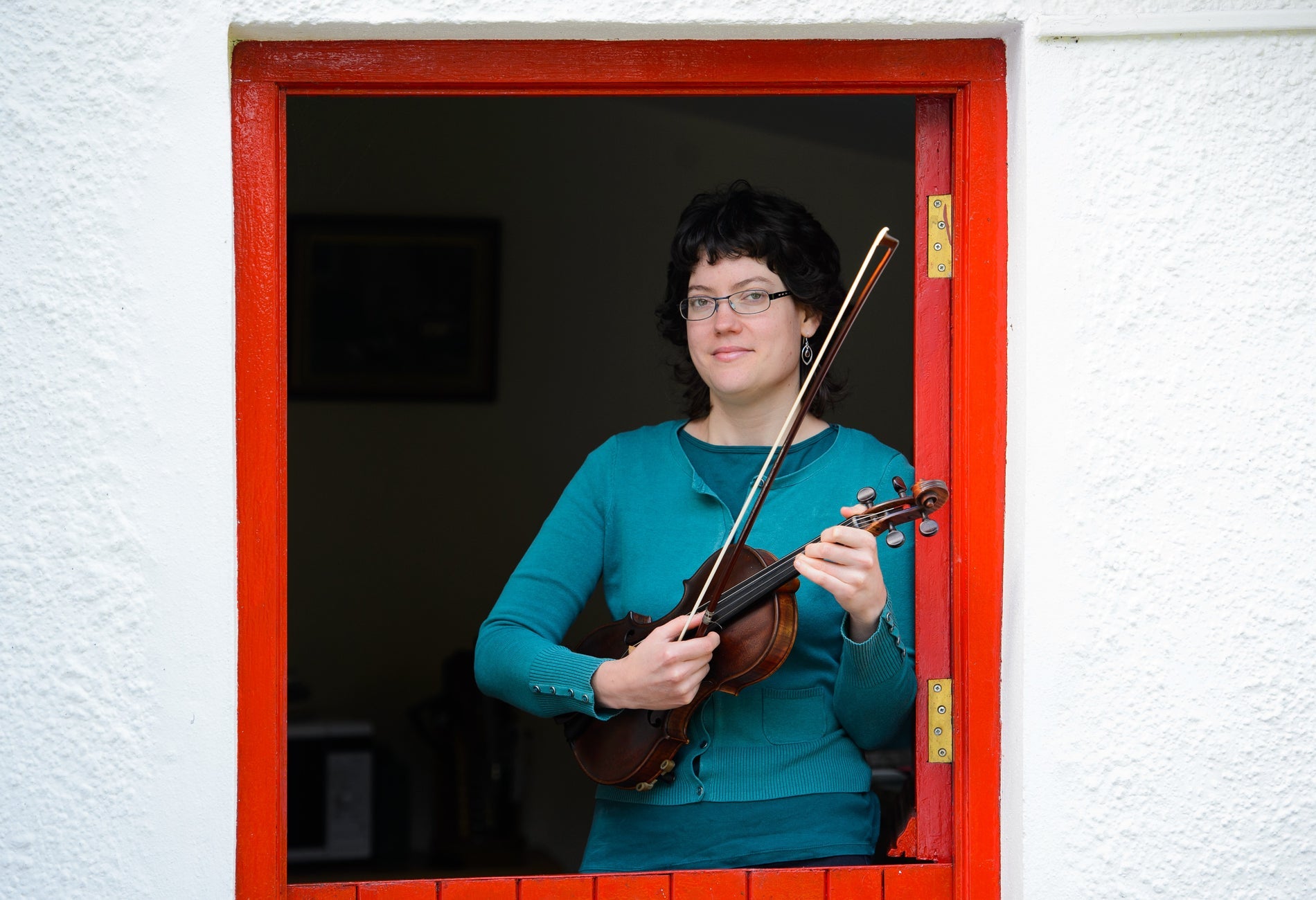 Person holding a fiddle in a red half doorway with the bottom half closed