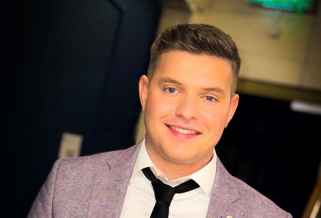 A smiling man in black tie and light grey jacket.