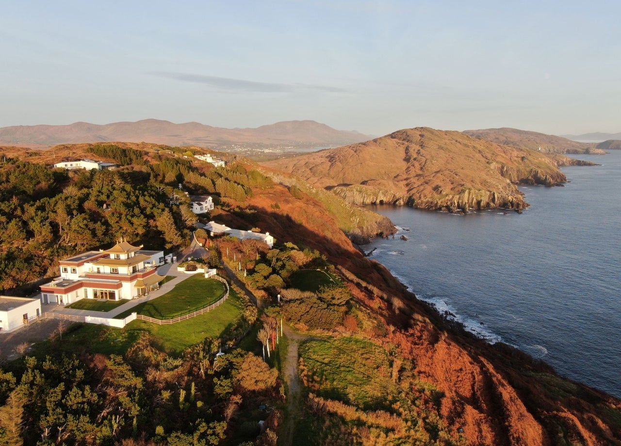 An aerial view of a building resembling a small Tibetan monastery perched on a cliff