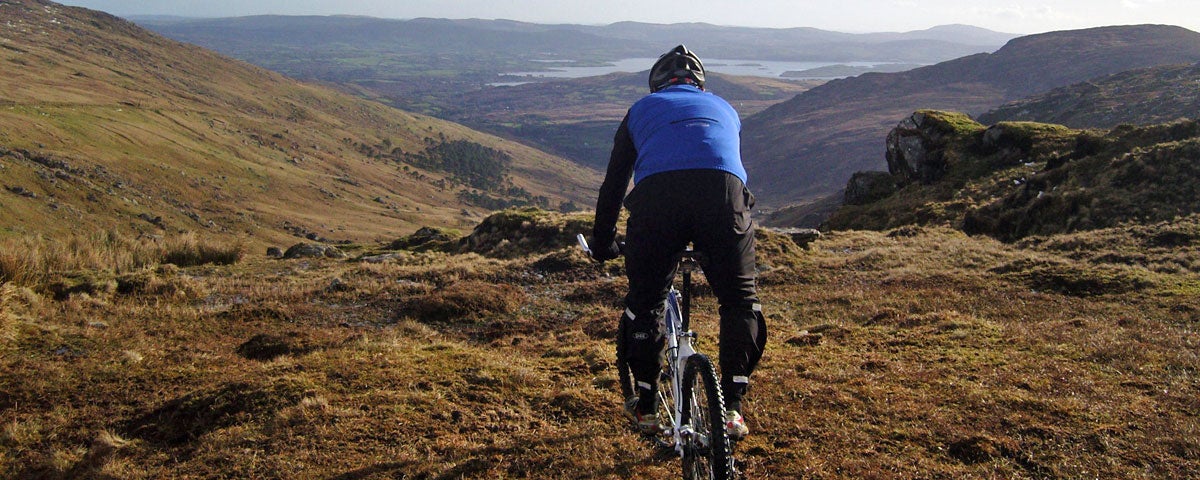 A man sitting on a mountain bike wearing a blue cycyling top looking out over a mountainscape expanse