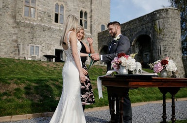 A bride and groom standing at a table with flowers outside a period house