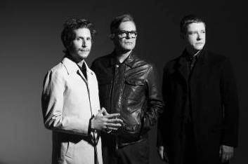 Black and white photo of 3 serious looking men against black background.