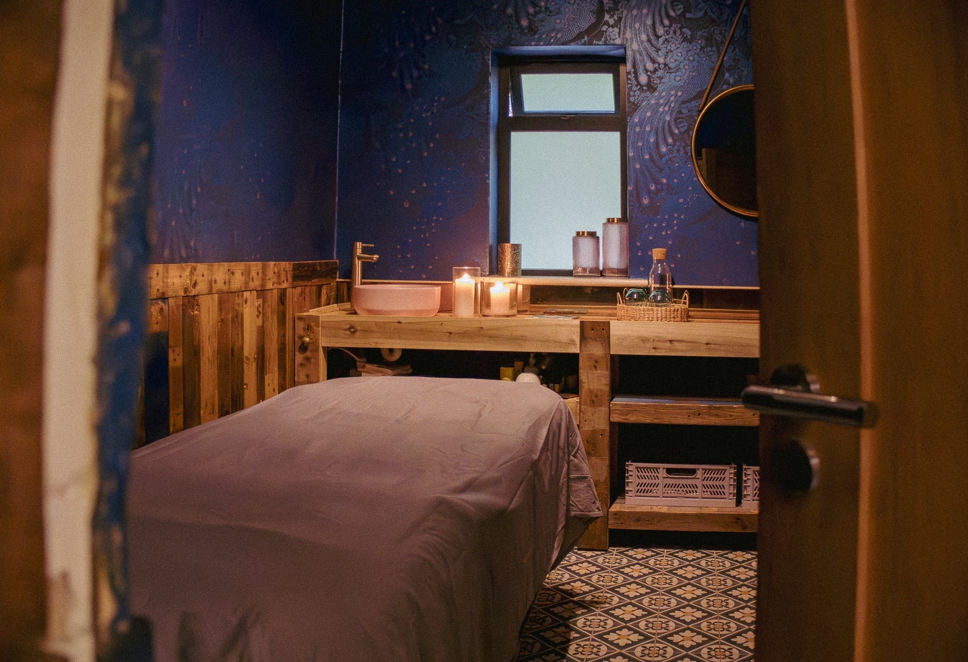 Spa treatment room with a table and pink basin and candles on wooden shelving