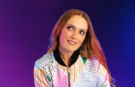 A woman smiling, looking upwards to her right, against plain blue to purple background.