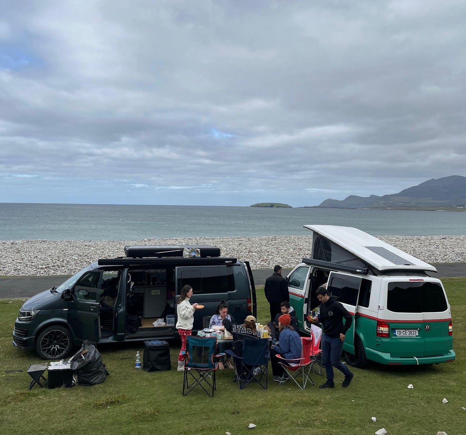 A group of people having a picnic beside two camper vans