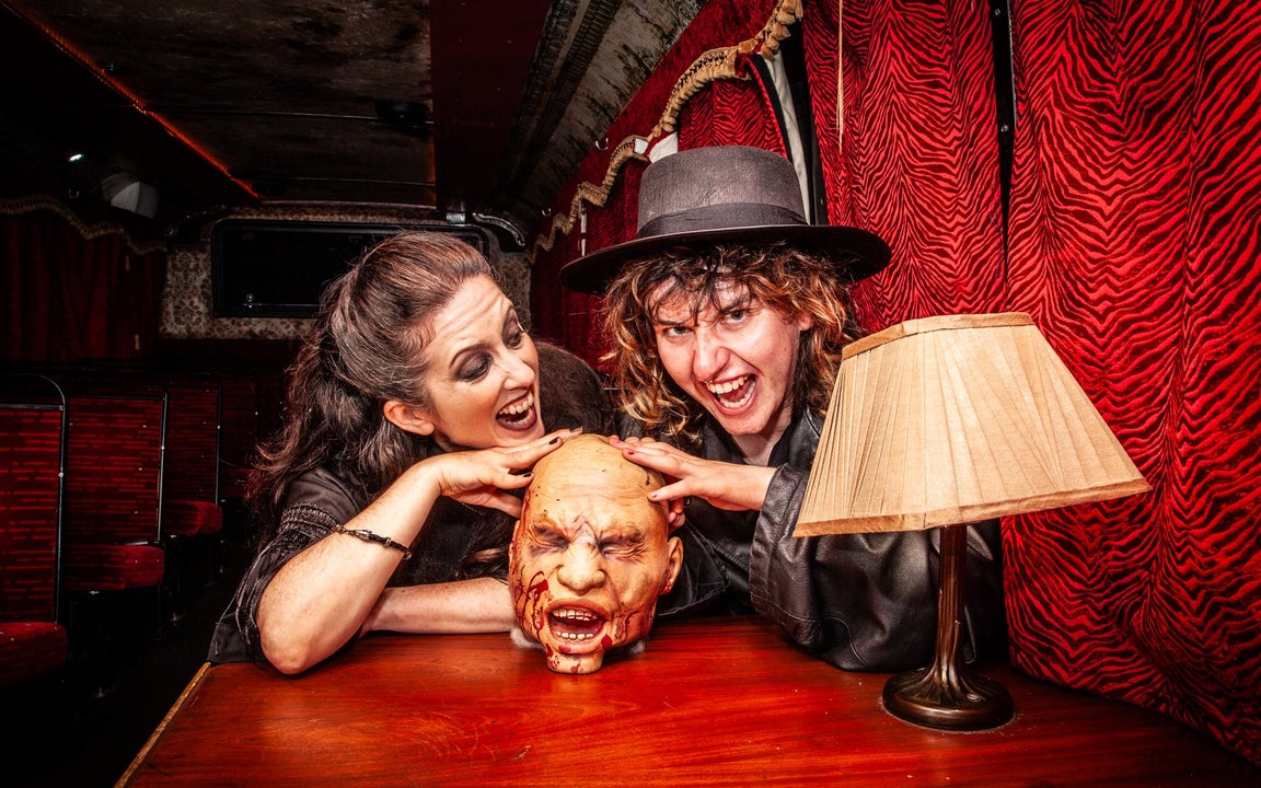 Two characters in costume with a disembodied model head on a table