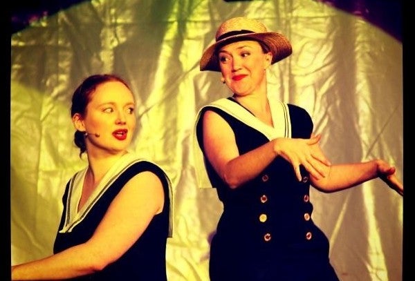 2 people in dark sailor style dresses are performing with gold background.