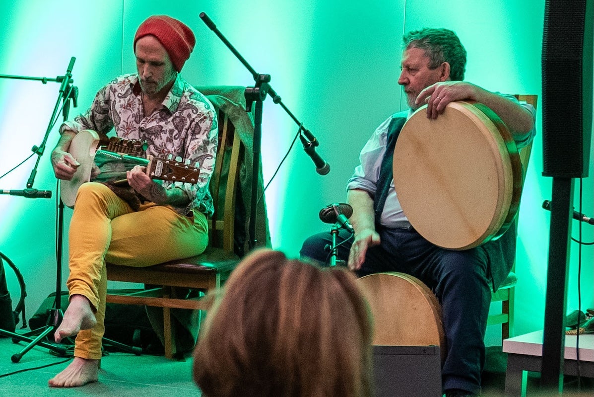 2 seated men with musical instruments on a small stage.