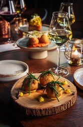 A glass of white wine on a table surrounded by a selection of small plate dishes