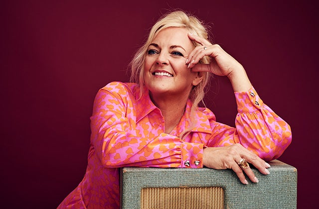 A smiling woman in pink shirt leaning on a table