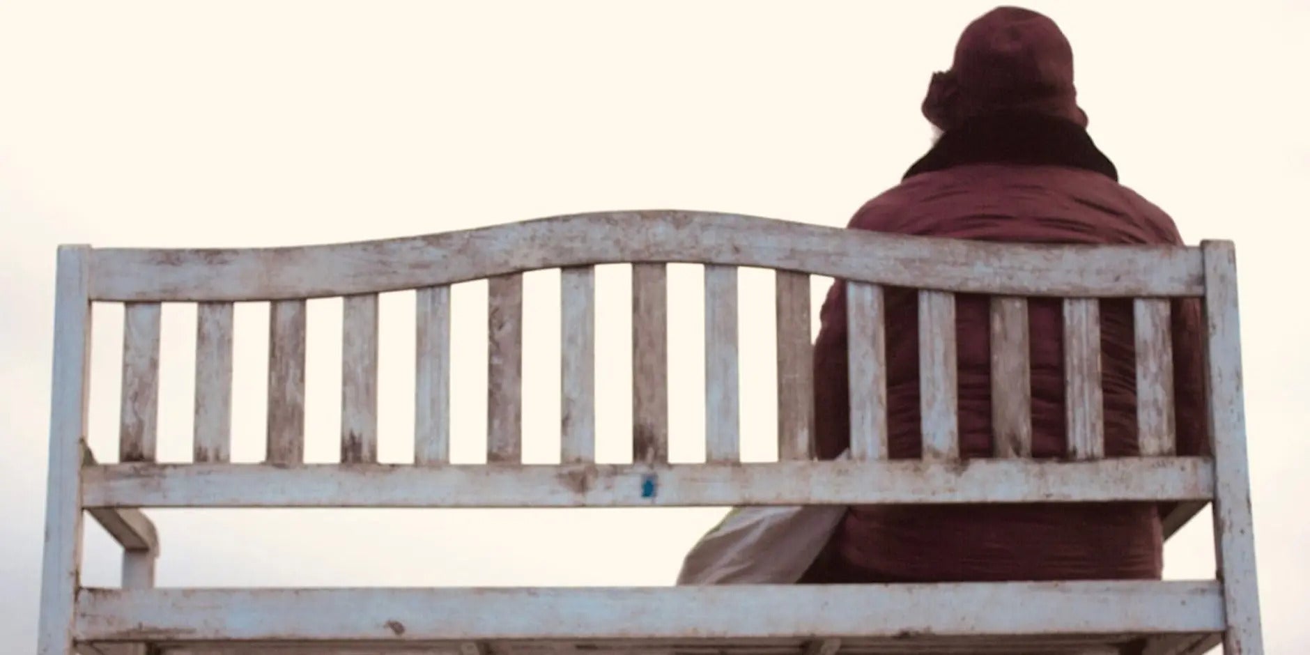 'An tÉalú' Ceoldráma Nua le Seán Óg Ó Duinnín - rear view of person in winter coat and hat seated at one end of a wooden bench.
