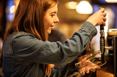 A woman behind a bar about the pull a pint