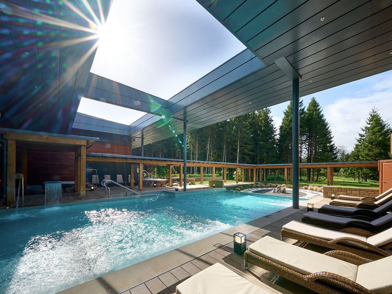 Outdoor pool surrounded by wooden decking and loungers with cushions