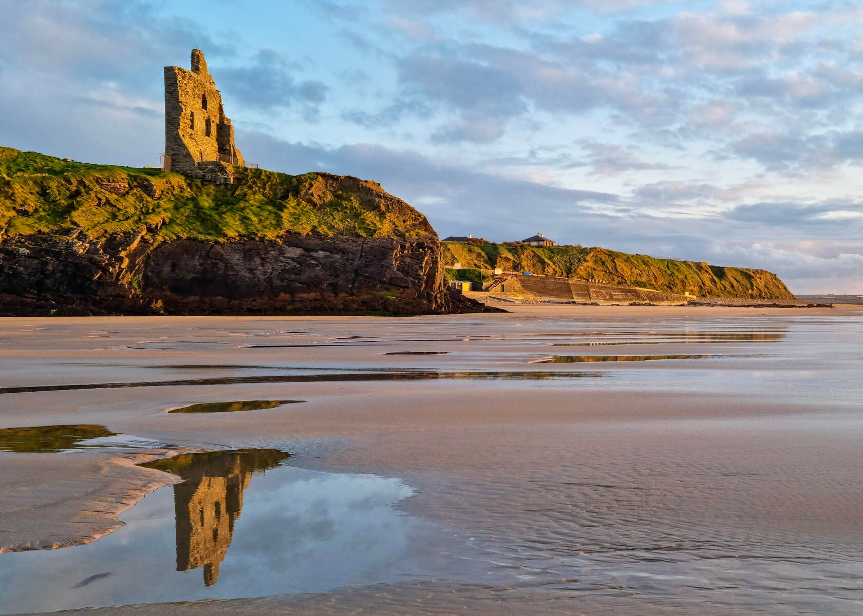 Ballybunion castle on cliff reflected in water on the beach below