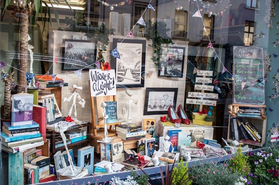 A shop window with lots of different books with paper figures, bunting and pictures in frames.