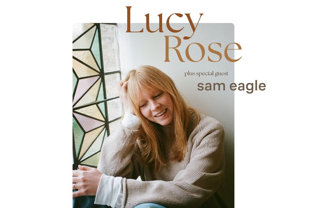 British songwriter Lucy Rose, a smiling woman leaning her head on one hand, looking downwards.