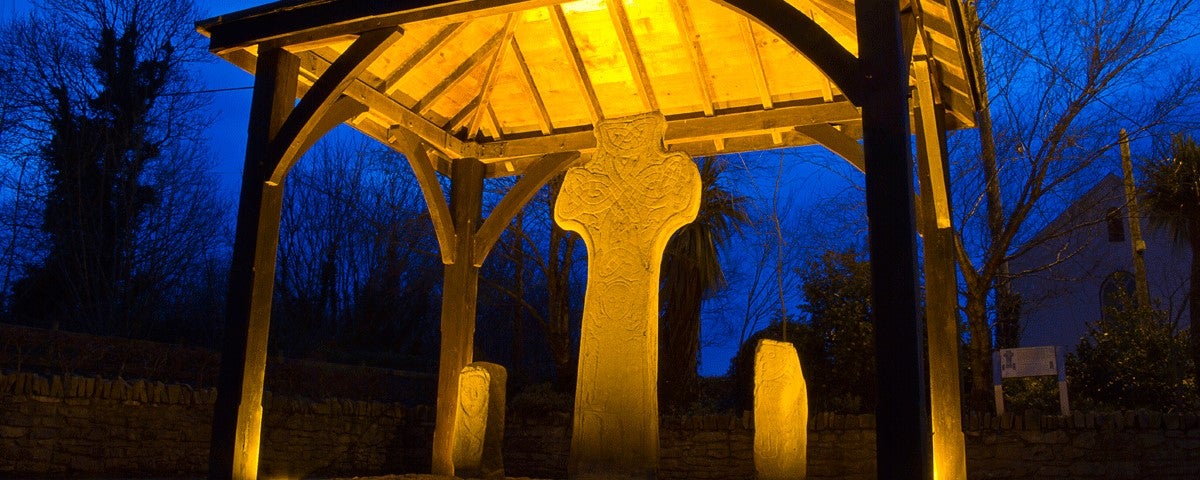 An ancient stone cross lit up at night