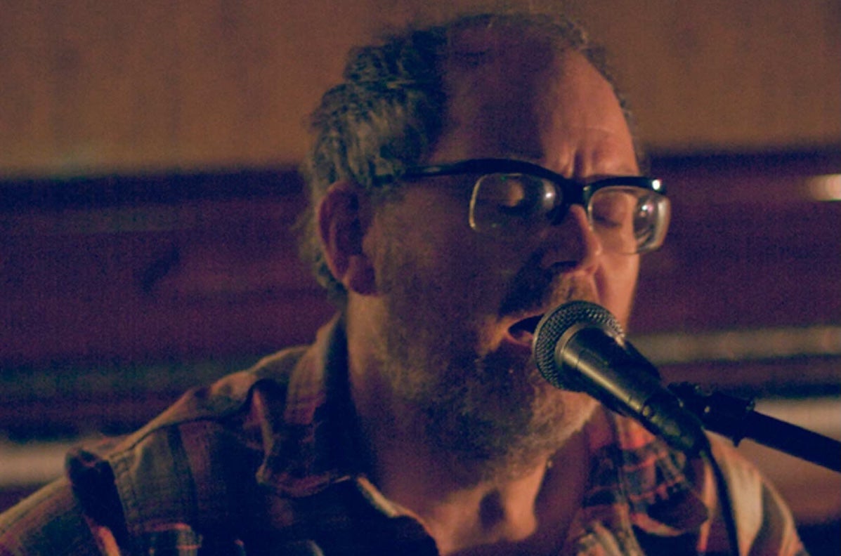 A darkly lit close up of man singing into a mic on a stand.