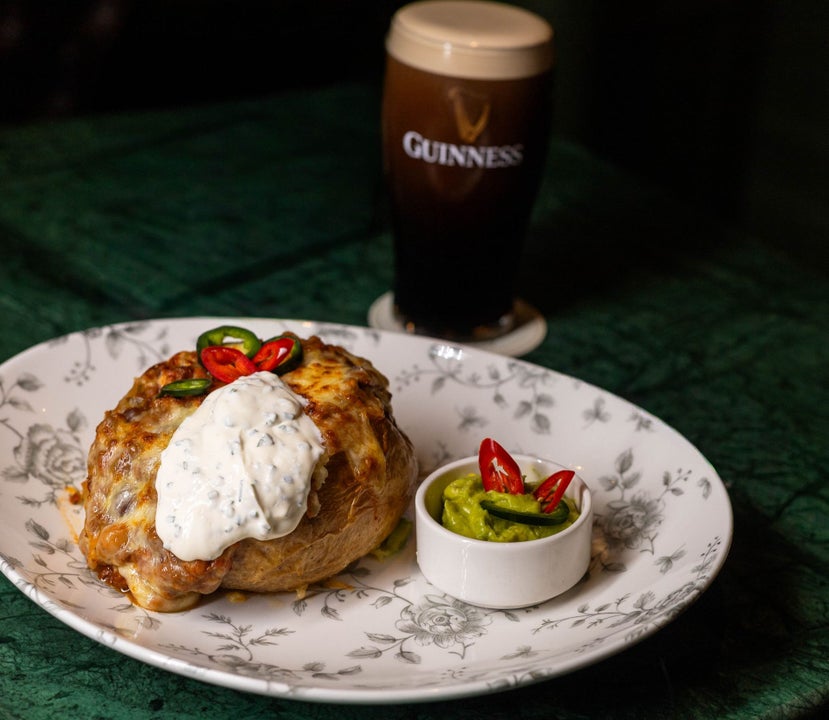 A main course served on a plate alongside a small bowl of green dip with a pint of Guinness in the background