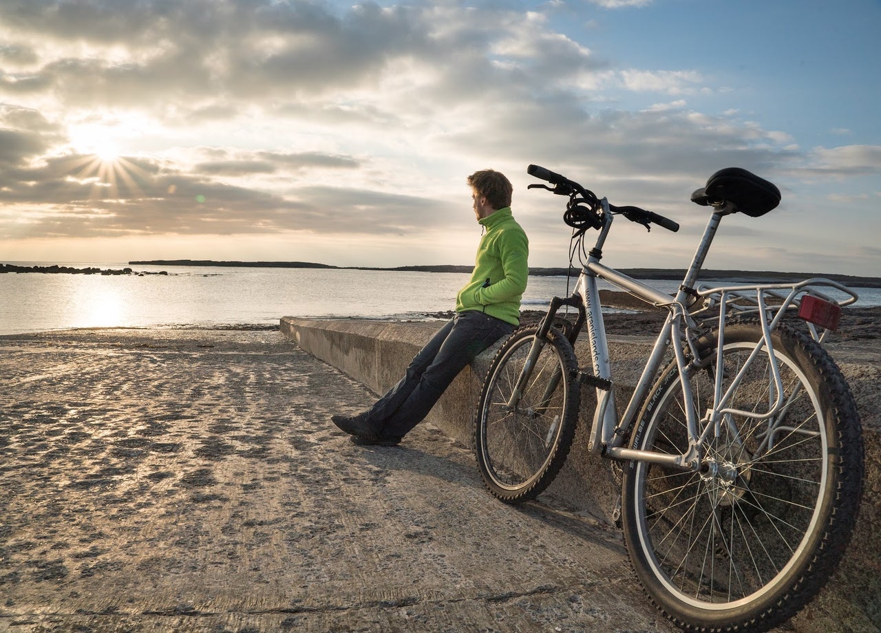 A man looking out to sea sitting on a beach next to his ebike from Ebike Aran Islands