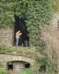 A person standing writing on a notebook within a dark opening in a historic stone structure