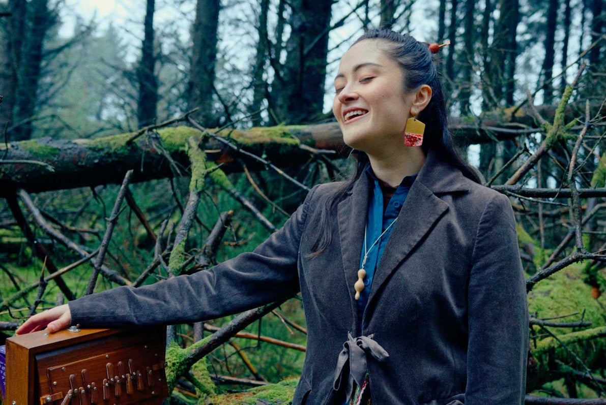A smiling woman with eyes closed, outdoors with bare trees behind.