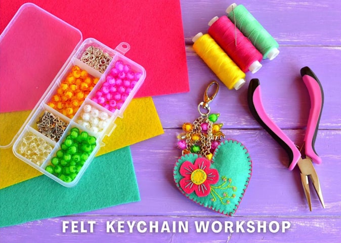 Looking down on a work surface with threads, pliers, a box with different coloured beads and a heart shaped keyring.