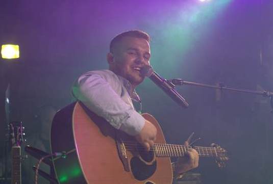 Singer, songwriter Dan McCabe playing a guitar and singing into mic on a stand.