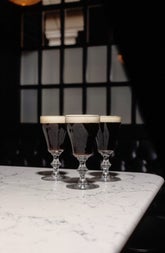 Three Irish coffee glasses sit on the corner of a white marble bar counter
