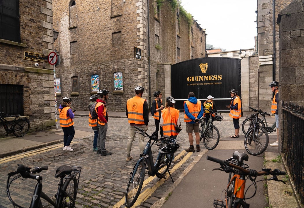 Group of people in orange high visibility vests on a cycling tour in front of the Guinness storehouse